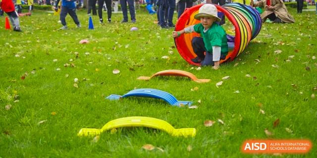 A young student crawling through a red arch on a green lawn during a fun outdoor activity or field day at Western International School of Shanghai.