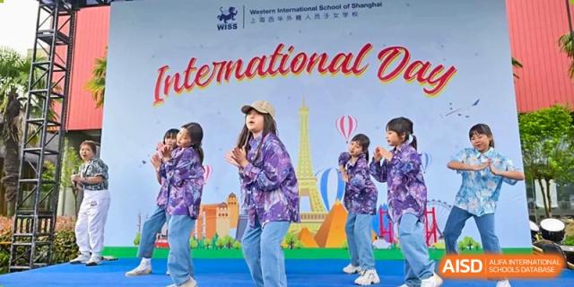 Students dressed in purple outfits performing a dance routine in front of a colorful banner during an International Day event at Western International School of Shanghai.