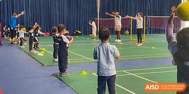 A group of young students participating in an indoor sports drill, running with paddles and cones, at Western International School of Shanghai.