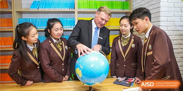 A male teacher helps two female students in brown uniforms study a large blue globe in a classroom at Yinghua Academy of Tianjin.