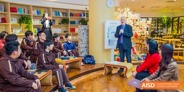 A male teacher presents to a small, seated group of students in a modern, well-lit classroom setting at Yinghua Academy of Tianjin.