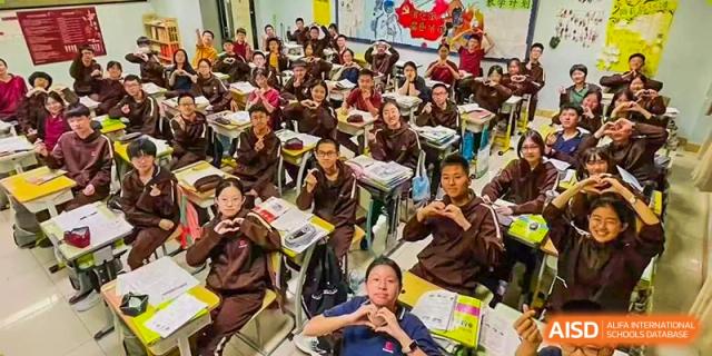 A large group of happy students and a teacher pose for a crowded group photo in a classroom at Yinghua Academy of Tianjin.