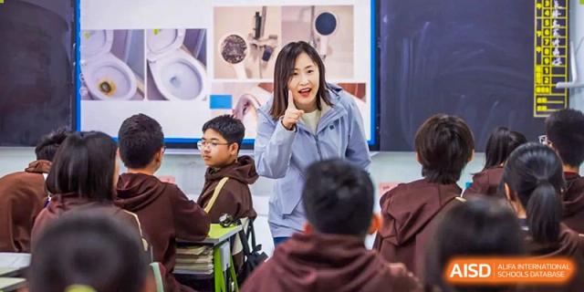 A female teacher in a light blue jacket enthusiastically addresses a group of students seated in a classroom at Yinghua Academy of Tianjin.