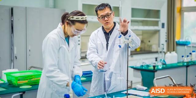 Two adults, one male and one female, wear lab coats and safety goggles while working with laboratory equipment at Yinghua Academy of Tianjin.
