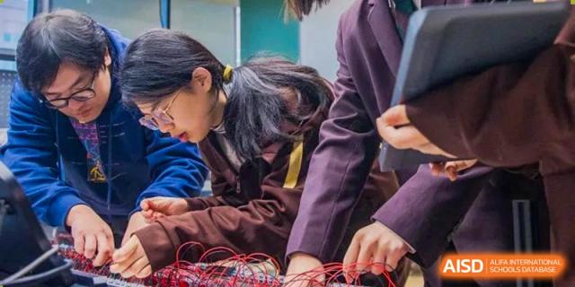 A student in a brown uniform leans over, focused on connecting small electronic components and wires during a class at Yinghua Academy of Tianjin.