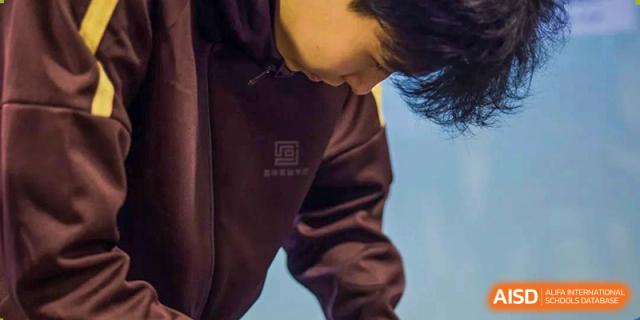 A close-up shot of a student wearing the brown school uniform jacket with the logo visible on the chest at Yinghua Academy of Tianjin.