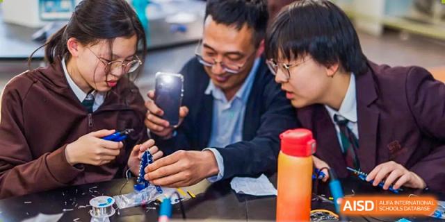 An adult male and a student observe something on a smartphone together while working on a technical project at Yinghua Academy of Tianjin.