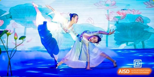 Two female dancers in light blue costumes performing a graceful dance on a brightly lit stage at Yinghua Academy of Tianjin.