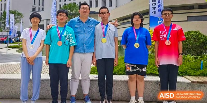 Four individuals, three wearing medals, posing for a group photo outdoors at Yinghua Academy of Tianjin.