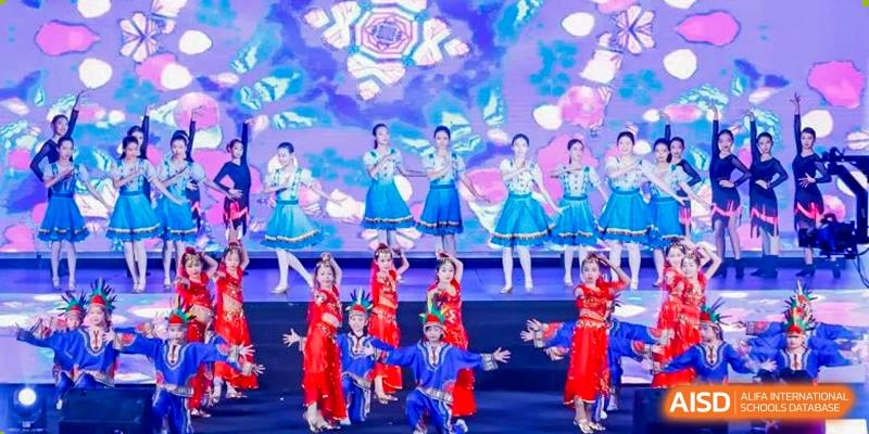 Students in colorful traditional costumes performing a folk dance on a bright stage at Yinghua Academy of Tianjin.