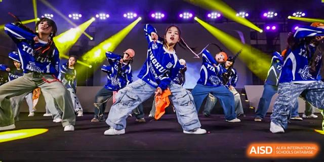 A student in blue and white baggy clothes performing a dynamic hip-hop dance on stage at Yinghua Academy of Tianjin.
