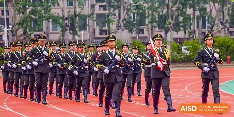Students in dark, formal uniforms marching in formation on a track during an event at Yinghua Academy of Tianjin.