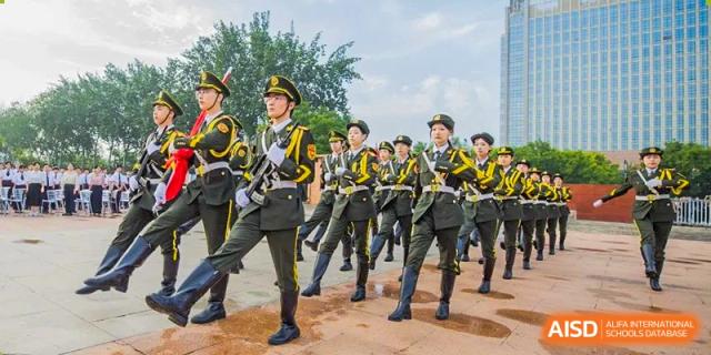 Students in formal uniforms marching in formation outdoors under a bright sky at Yinghua Academy of Tianjin.