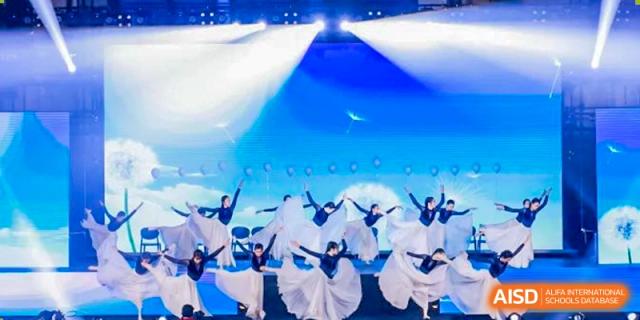 A group of students performing a synchronized modern dance in white flowing costumes on a brightly lit stage at Yinghua Academy of Tianjin.