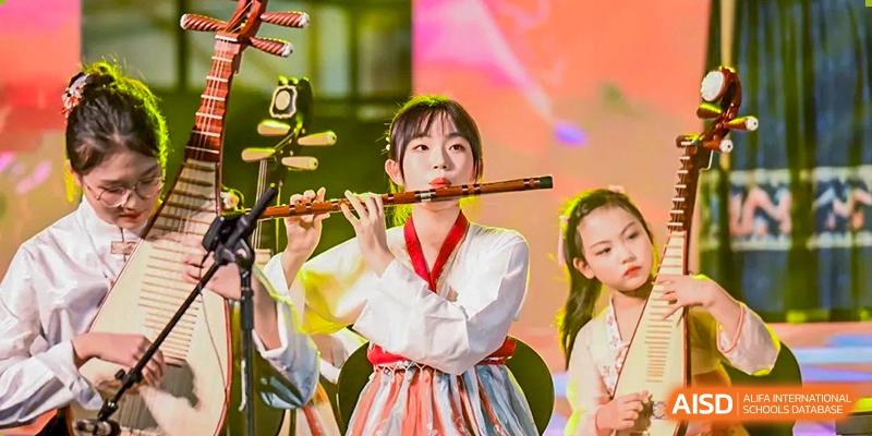 A female student in traditional clothing playing a flute on stage during a cultural performance at Yinghua Academy of Tianjin.
