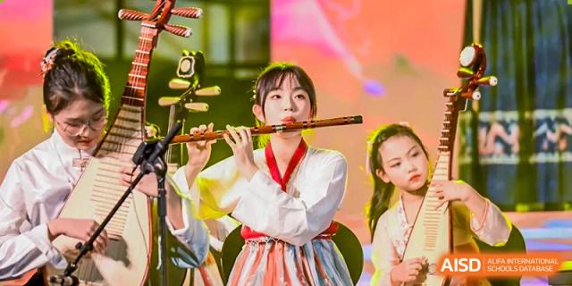A female student in traditional clothing playing a flute on stage during a cultural performance at Yinghua Academy of Tianjin.