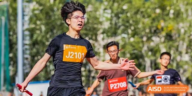 A male student wearing a race bib (J2101) running in an outdoor race, focusing on the finish line at Yinghua Academy of Tianjin.