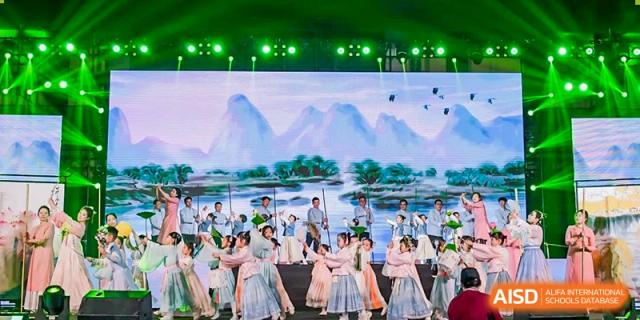 Students in traditional costumes performing on a stage with a scenic mountain backdrop at Yinghua Academy of Tianjin.