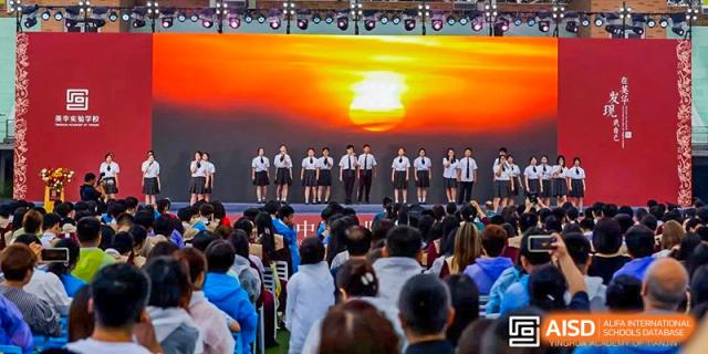 Students in uniform standing in front of a dramatic sunset backdrop during a school assembly or event at Yinghua Academy of Tianjin.