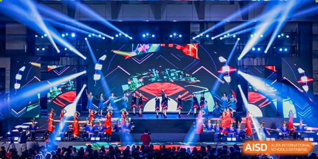 Students performing a dynamic routine on a bright stage with large screens during a school event at Yinghua Academy of Tianjin.