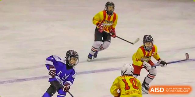 Students playing ice hockey, wearing protective gear and uniforms, during a sports competition at Yinghua Academy of Tianjin.