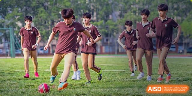 Students in dark brown gym uniforms running and playing a field sport outdoors at Yinghua Academy of Tianjin.