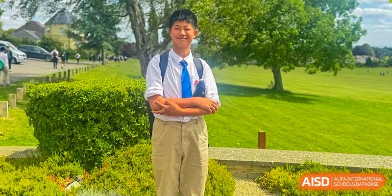 Portrait of a smiling male student in a white shirt and tie standing on a sunny lawn at Suzhou Science and Technology Town Foreign Language High School.