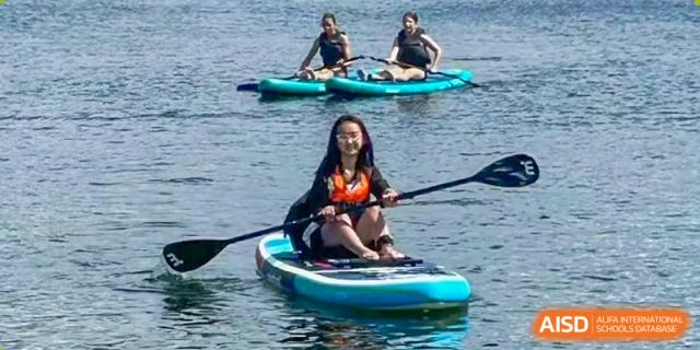 A student sits on a paddle board in the water, holding a paddle, with other students in the background. Suzhou Science and Technology Town Foreign Language High School.