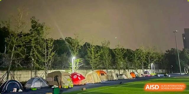 Tents set up outdoors near a grassy field and trees at night, suggesting a school camping activity. Suzhou Science and Technology Town Foreign Language High School.