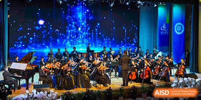 An orchestra performing on a stage with bright blue lighting, showcasing a musical event at Suzhou Science and Technology Town Foreign Language High School.