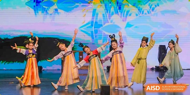 Four female students performing a colorful traditional dance on a stage at Suzhou Science and Technology Town Foreign Language High School.