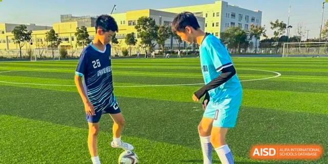 Two male students practicing soccer skills on a bright green field at Suzhou Science and Technology Town Foreign Language High School.