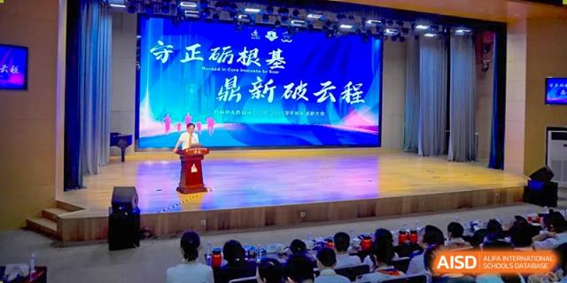 A speaker on a stage addressing an audience in a hall during a ceremony at Suzhou Science and Technology Town Foreign Language High School.