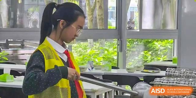 A female student in a safety vest and glasses focused on a task near a window at Suzhou Science and Technology Town Foreign Language High School.
