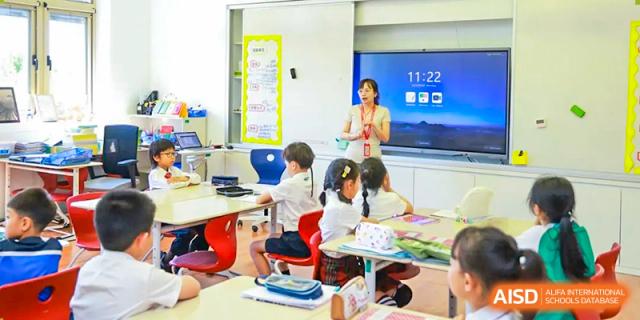 A teacher at Dehong Beijing International Chinese School instructs primary students in a bright classroom using a smart screen.