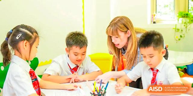 A female teacher at Dehong Beijing International Chinese School is helping a young male student with his work at a desk.