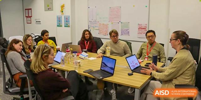 Teachers or staff members at Dehong Beijing International Chinese School collaborating in a meeting room, using laptops.