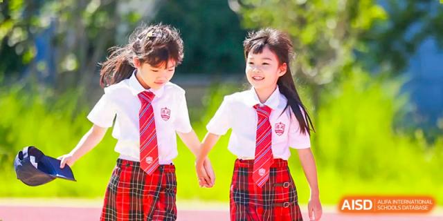 Two happy, young female students at Dehong Beijing International Chinese School walking hand-in-hand, wearing school uniforms.