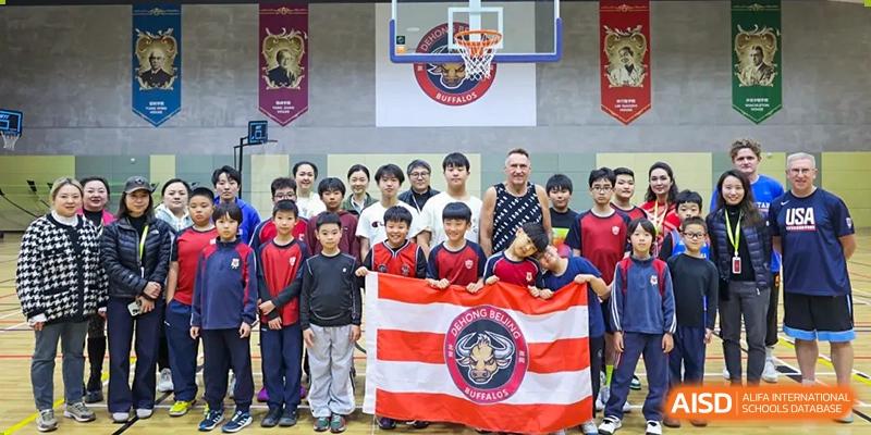 Students and coaches at Dehong Beijing International Chinese School posing for a team photo on the basketball court, holding a school flag.