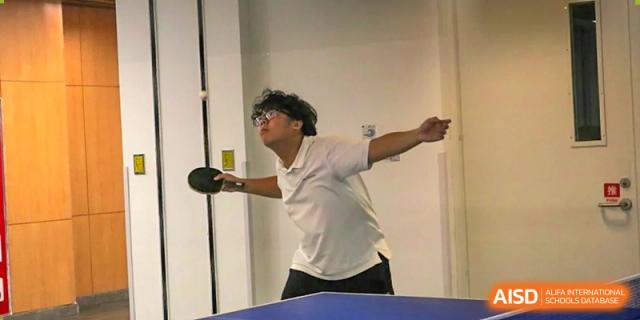 A student at Dehong Beijing International Chinese School playing table tennis in an indoor sports area, focused on the ball.