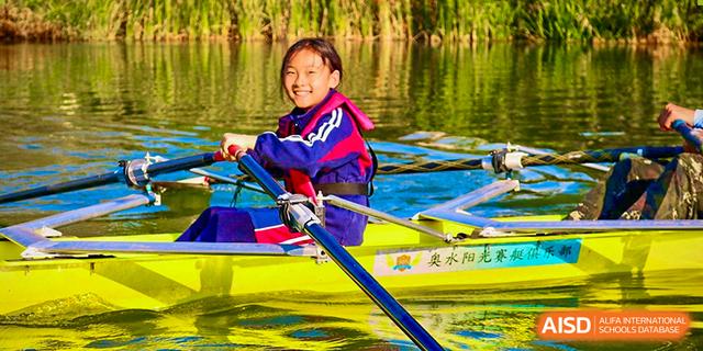 A smiling student from Dehong Beijing International Chinese School rowing a bright yellow boat on a sunny day.
