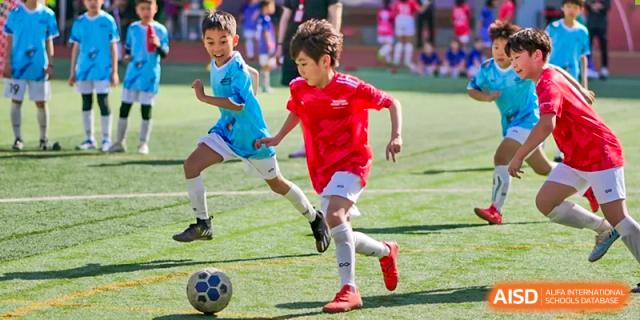 A close-up of two students from Dehong Beijing International Chinese School competing for the ball during an intense football (soccer) match.