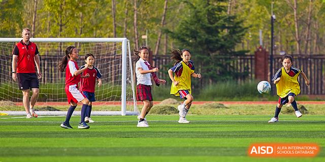 Students from Dehong Beijing International Chinese School practicing or playing football (soccer) on a bright green sports field.