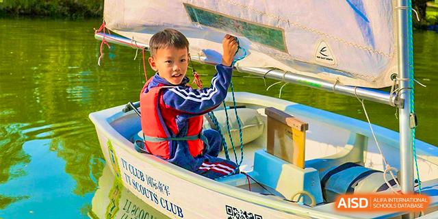 A young student from Dehong Beijing International Chinese School happily paddling a small boat while wearing a life vest.