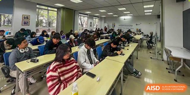 Students are seated at desks, engaged in a lesson in a brightly lit lecture room at Cambridge International School Litai College. SISU.