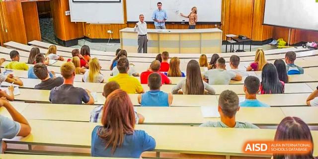 A large lecture hall with students seated facing the front where two speakers are standing at Cambridge International School Litai College. SISU.