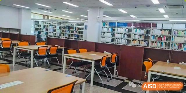 A view of library seating areas with tables, orange chairs, and surrounding bookshelves at Cambridge International School Litai College. SISU.