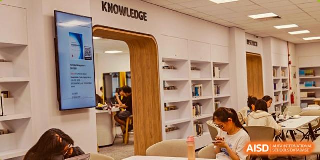 A student reads in a well-lit library area with a distinctive 'KNOWLEDGE' archway and bookshelves at Cambridge International School Litai College. SISU.