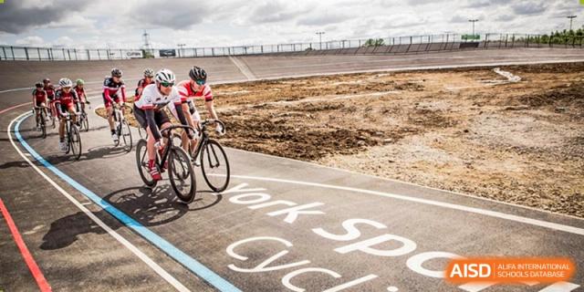 A cyclist rides on an asphalt outdoor track where the words "Work Space Cycle" are painted, next to a dirt infield at Cambridge International School Litai College. SISU.