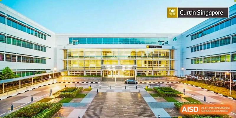 A modern school building with a bright yellow and glass exterior dominates the view, looking across a wide, paved entrance courtyard at Cambridge International School Litai College. SISU.